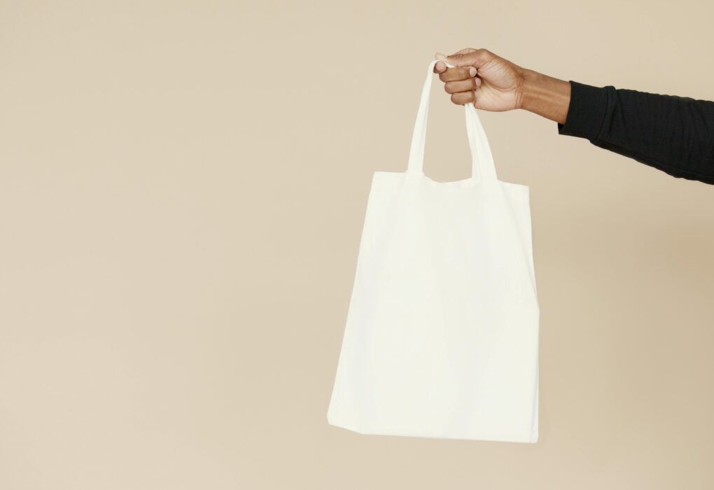 Stylish and simple white tote bag held by a hand against a neutral background, perfect for branding or eco-friendly themes.