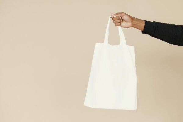 Stylish and simple white tote bag held by a hand against a neutral background, perfect for branding or eco-friendly themes.